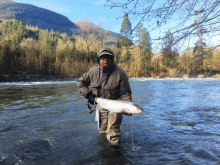 a man in a hooded jacket holds a large fish in a river