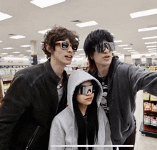 a woman wearing a hoodie and sunglasses poses for a photo with two men