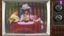 a television screen shows a picture of a woman sitting at a table with two children .