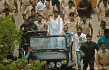 a man in a white shirt stands in front of a crowd of police officers and a jeep with stars on the front