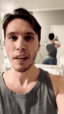 a man in a grey tank top is taking a picture of himself in front of a mirror