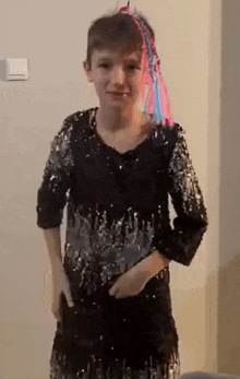 a young boy is wearing a black sequined dress with a pink and blue ponytail on his head .