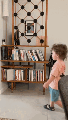 a little boy is walking in front of a bookshelf with books on it including one titled " a brief history of time "