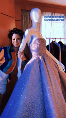 a woman adjusts a blue dress on a mannequin with a caption that says kissesdelay