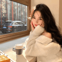 a woman in a white sweater sits at a table with a cup of coffee