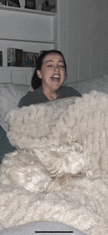 a woman is laughing while laying on a couch with a white dog