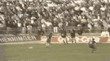 a group of people are playing soccer on a field with a sign that says henniger in the background .