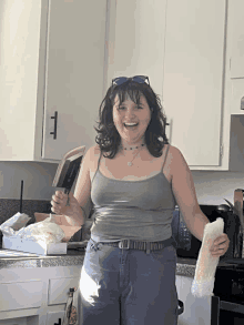 a woman wearing sunglasses and a grey tank top smiles while holding a sandwich