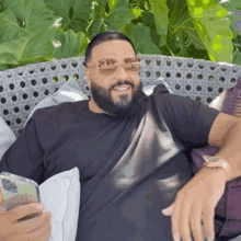 a man with a beard is sitting on a couch holding a cell phone and smiling .