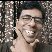 a man wearing glasses and a black shirt is smiling with his hand on his chin