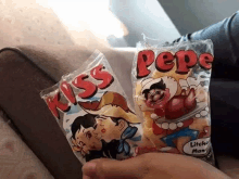 a person holding two bags of kiss pepe candy