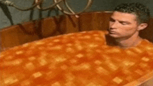 a man is taking a bath in a bathtub filled with a large orange pie .