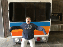 a boy wearing a gap sweatshirt is standing in front of a bus