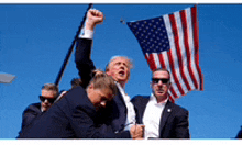 a man in a suit holds up his fist while another man holds an american flag