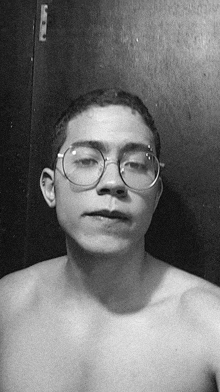 a shirtless man wearing glasses looks at the camera