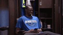 a man in a blue minnesota shirt is sitting in a chair looking at his phone