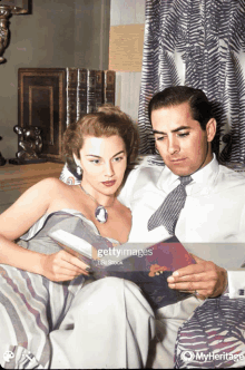 a man and woman are sitting on a bed reading a book