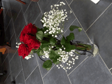 a vase filled with red roses and baby 's breath on a tiled floor