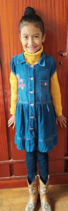 a little girl wearing a blue dress and cowboy boots smiles for the camera