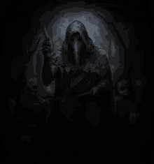 a man in a hooded cloak is holding a knife in a dark forest .