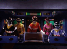 a group of power rangers are standing next to each other in a room with a monitor .