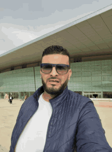 a man wearing sunglasses and a blue jacket takes a selfie in front of a building