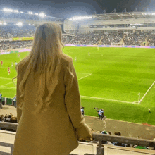 a woman is watching a soccer game in a stadium with a yellow sign that says ' coca cola ' on it