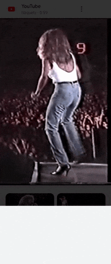 a woman in a white tank top and blue jeans is dancing in front of a crowd on youtube