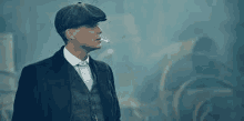 a man in a suit and hat is smoking a cigarette in the fog .