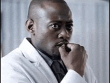 a man in a white coat and tie is biting his nails and looking at the camera .