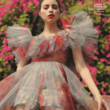 a woman in a red and grey dress is standing in front of a bush with pink flowers and the words lakme fashion week next to her