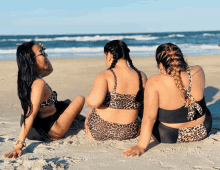 three women in leopard print bikinis sitting on the beach