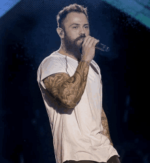 a man with a beard is singing into a microphone while wearing a white shirt