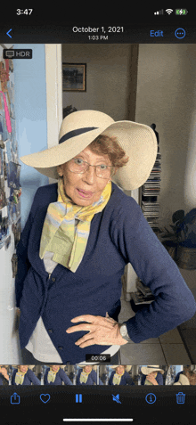 an older woman wearing a hat and scarf is standing in front of a door on october 1st