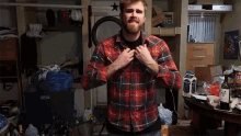 a man in a plaid shirt is standing in a messy room with a bottle of jack daniels on the table