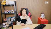 a woman sits at a desk in front of a microphone with a cube logo on the wall behind her