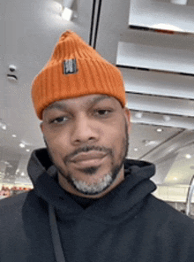 a man with a beard wearing an orange beanie and a black hoodie .