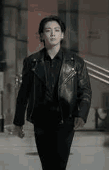 a man in a black leather jacket and black shirt is walking down a street .