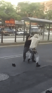 two people are fighting on the side of a street