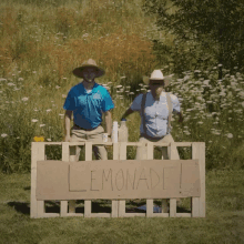 two men are standing behind a lemonade stand