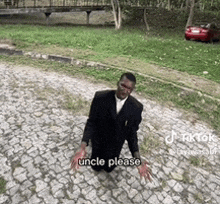 a man in a suit is kneeling down on a cobblestone road and says uncle please .