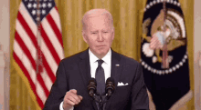 a man in a suit and tie is giving a speech in front of two microphones in front of an american flag .