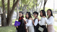 a woman in a graduation cap and gown holds a purple folder that says ' thailand ' on the top