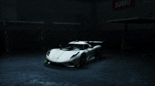 a white sports car is parked in a dark garage with a sumo sign in the background