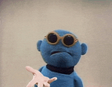 a blue stuffed animal wearing sunglasses is reaching out towards a person .