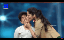 a woman kisses another woman on the cheek in front of a television screen that says mallemala tv