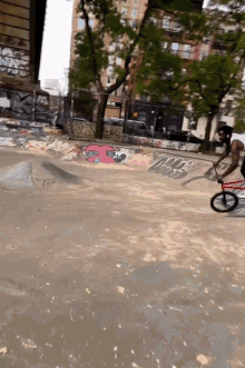 a man is riding a bike on a dirt road with graffiti on the wall that says ' a ' on it