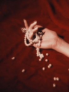 a woman 's hand is holding a pearl necklace on a red surface .