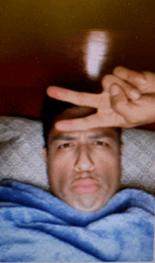 a man laying in bed making a peace sign with his hands