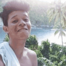 a young man with a towel wrapped around his neck is smiling in front of a body of water .